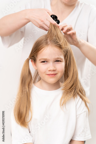woman combs and does the hair of a little girl on a white background.