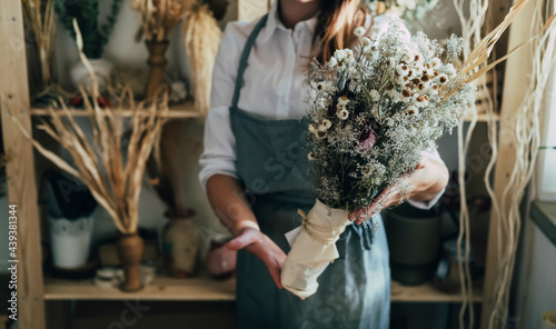 Unrecognizable Female Florist Holding Everlasting Bouquet of Different Dried Flowers at her Flower Shop. Close up photo of woman entrepreneur showing decorative bouquet with dry flowers and plants.