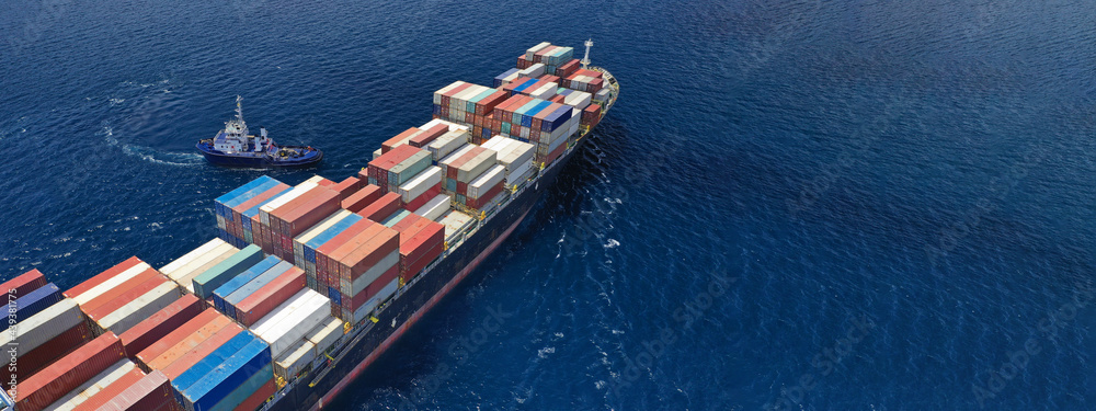 Fototapeta premium Aerial drone ultra wide top down photo of tow - tug boat assisting by pulling or pushing container ship to anchor in terminal port