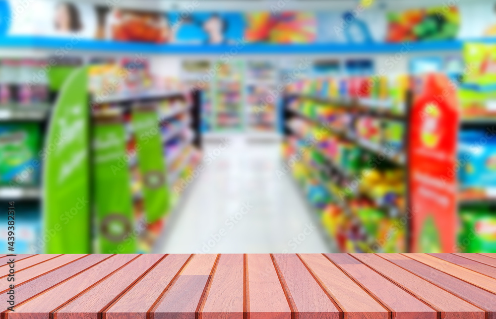 Empty wooden counter with blurred background of various goods on shelves inside of convenience store