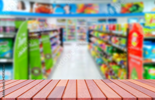 Empty wooden counter with blurred background of various goods on shelves inside of convenience store