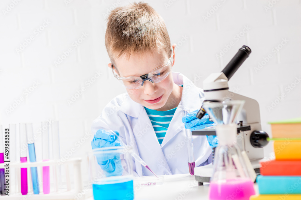 A schoolboy with a microscope examines chemicals in test tubes, conducts experiments - a portrait on a white background. Concept for the study of coronavirus in the laboratory A schoolboy with a microscope examines chemicals in test tubes, conducts experiments - a portrait on a white background. Concept for the study of coronavirus in the laboratory