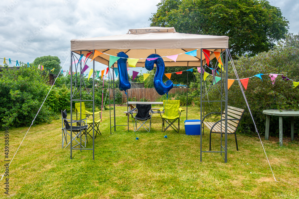 A gazebo setup and decorated with colourful bunting and blue helium '12' balloons ready for a twelfth birthday party in the garden. A gazebo setup and decorated with colourful bunting and blue helium '12' balloons ready for a twelfth birthday party in the garden.