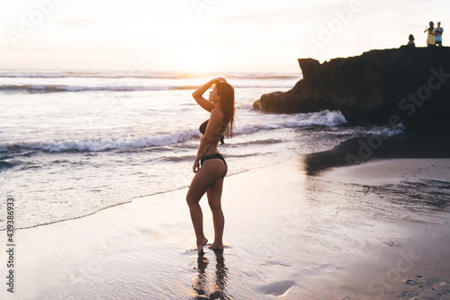 Slim woman touching hair while standing on wet sandy coast