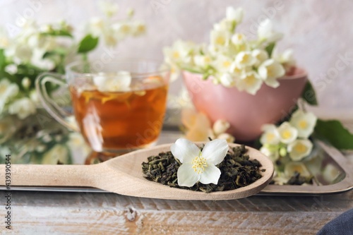 Cup of green tea, jasmine flowers on the table, ingredients of a healthy drink