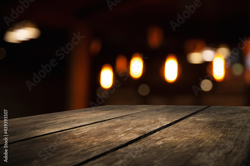 empty wooden table on blurred light gold bokeh of cafe-restaurant window on dark background, place for your products, blurred cafe interior.