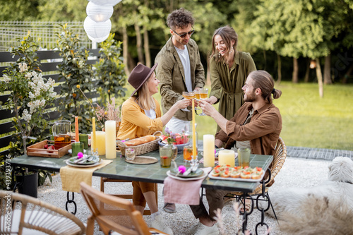 A group of young friends have delicious dinner, toasting and having great summertime together at the backyard of the country house in nature