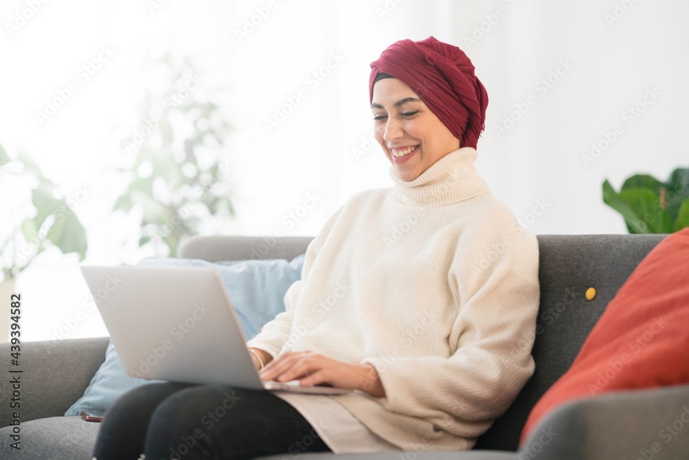 Smiling Muslim businesswoman working on laptop from home Smiling Muslim businesswoman working on laptop from home