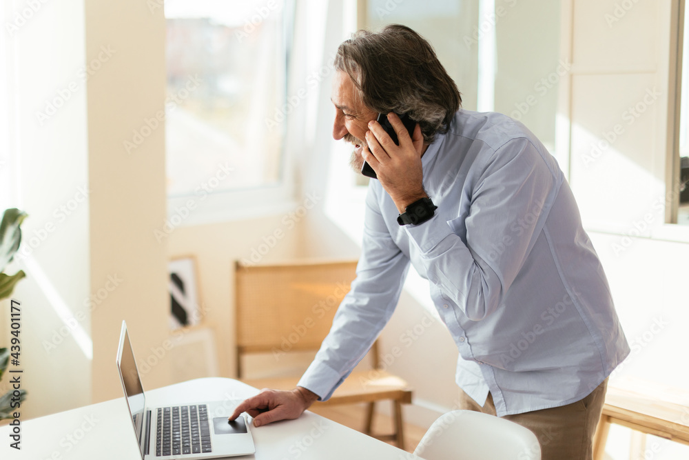 © BONNINSTUDIO/Stocksy - Mature freelancer talking on smartphone and using laptop