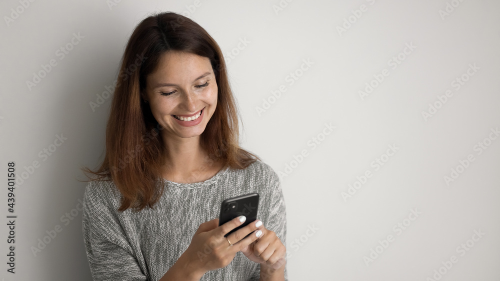 Close up smiling woman using smartphone on grey studio background isolated, happy young attractive female looking at phone screen, writing message in social network, chatting or shopping online Close up smiling woman using smartphone on grey studio background isolated, happy young attractive female looking at phone screen, writing message in social network, chatting or shopping online