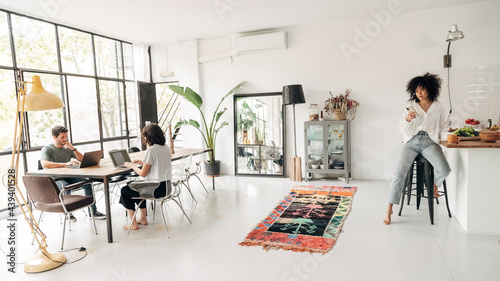 Young people working on laptop typing. Girl having coffee looking at cellphone. Big bright co working loft space photo