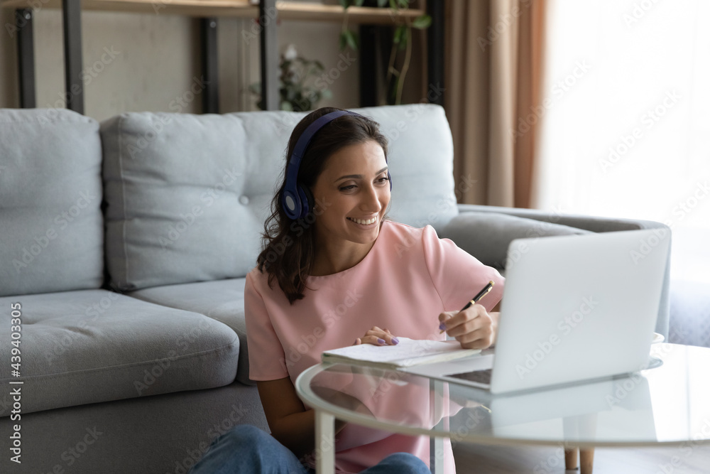Smiling Arabian woman in headphones using laptop, writing taking notes, motivated positive young female student watching webinar, involved in online course, studying at home, preparing to exam Smiling Arabian woman in headphones using laptop, writing taking notes, motivated positive young female student watching webinar, involved in online course, studying at home, preparing to exam