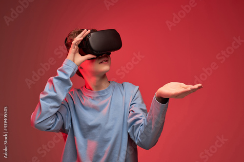 Young boy getting experience using VR-headset glasses of virtual reality in studio much gesticulating hands, excited boy in casual wear, playing virtual reality games