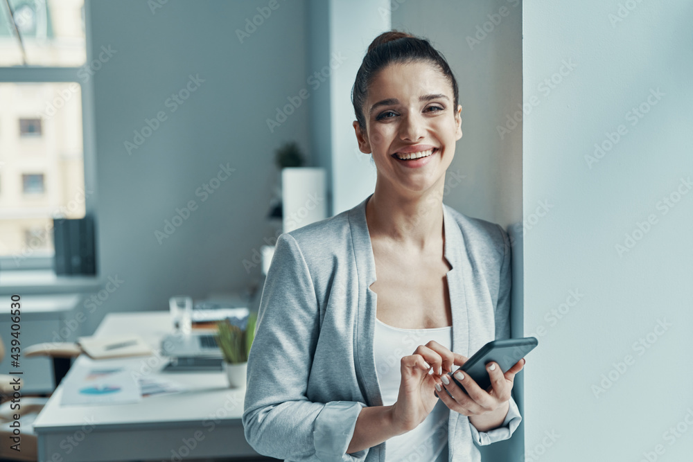 Beautiful young woman in smart casual using smart phone and smiling Beautiful young woman in smart casual using smart phone and smiling