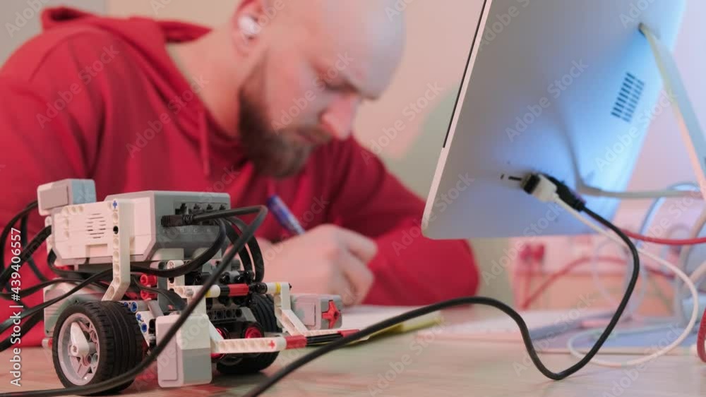 Close up of an young man that is learning robotics lessons using computer, writting notice in his notebook. Online courses and distance learning concept. Close up of an young man that is learning robotics lessons using computer, writting notice in his notebook. Online courses and distance learning concept.