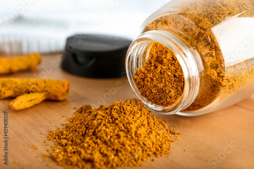 Jar with turmeric powder and roots on wooden background, closeup