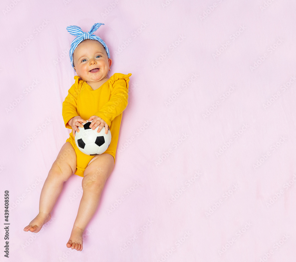 Fototapeta premium Laughing baby girl lay with football ball in bed