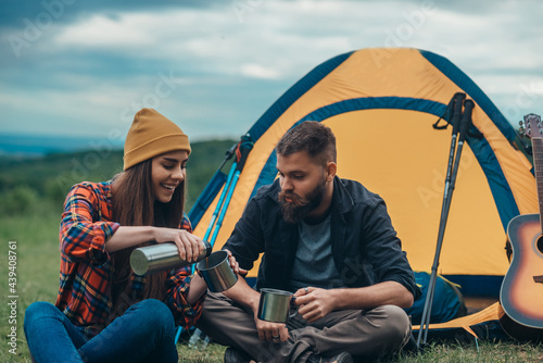 Young couple of campers drinking coffee from metal cups in the nature