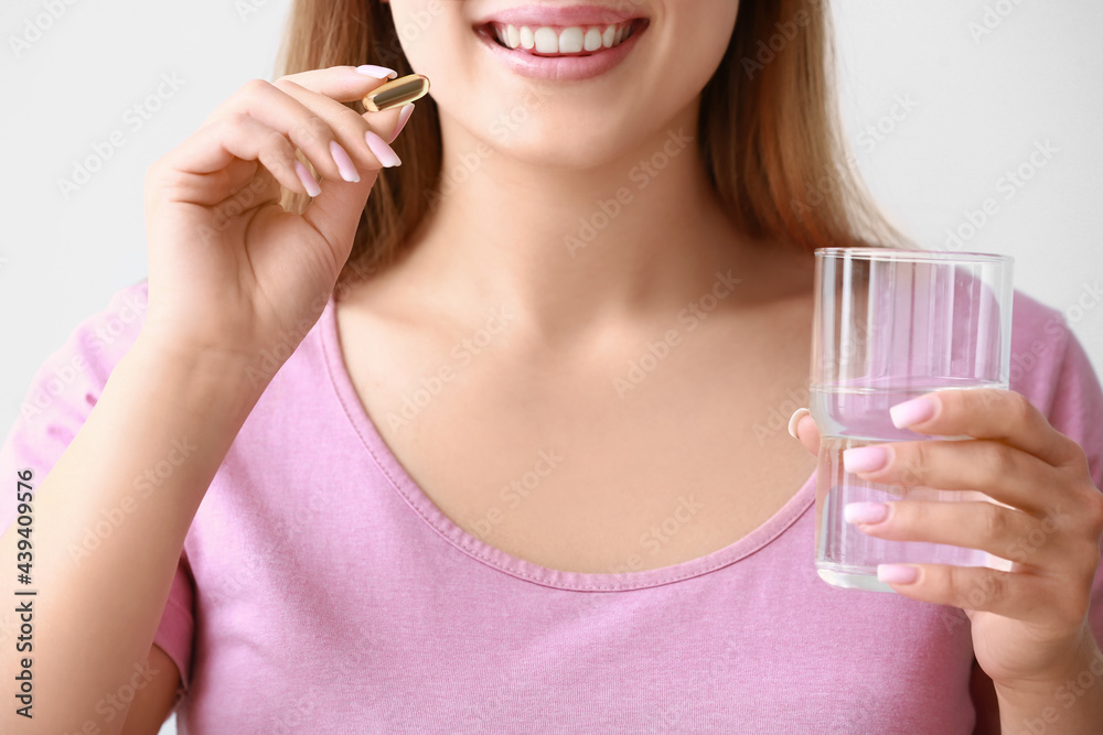 Young woman with fish oil pill on light background, closeup Young woman with fish oil pill on light background, closeup