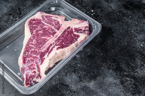 T-bon raw beef steak in vacuum packaging. Black background. Top view. Copy space