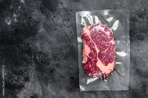 Raw rib eye beef meat steak in vacuum packaging. Black background. Top view. Copy space