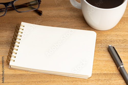 Spiral notepad mockup template with coffee cup and eyeglasses on wooden table. Empty White paper
