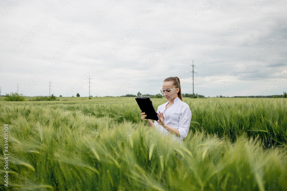 Young female ecologist scientist in goggles standing in green field and working on glass transparent screen Young female ecologist scientist in goggles standing in green field and working on glass transparent screen