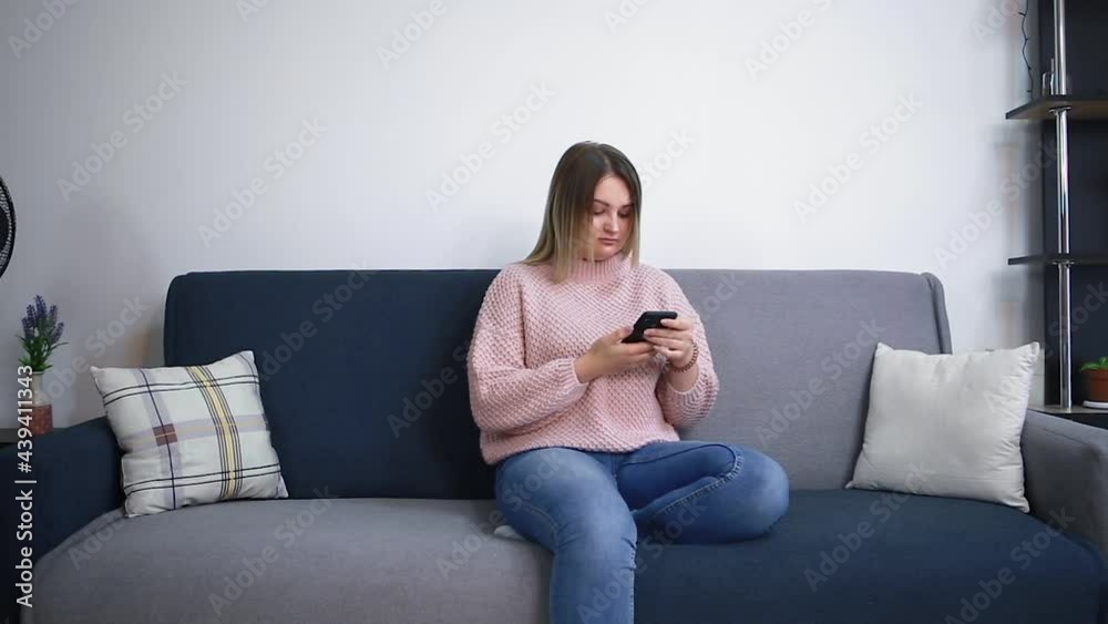 Young woman using smartphone, browsing social networks, checking news, sending text messages while sitting on the couch. A woman spends time at home with mobile gadgets. Young woman using smartphone, browsing social networks, checking news, sending text messages while sitting on the couch. A woman spends time at home with mobile gadgets.