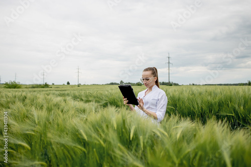 Slika na platnu Young female ecologist scientist in goggles standing in green field and working