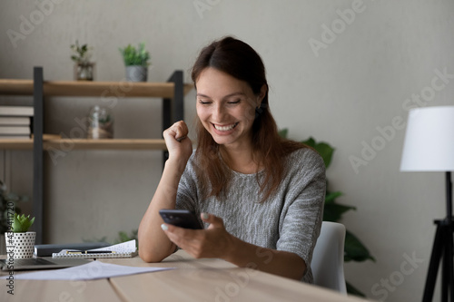 Excited woman reading good news, using smartphone, showing yes gesture, happy young businesswoman looking at phone screen, celebrating success, received job promotion or reward, business achievement