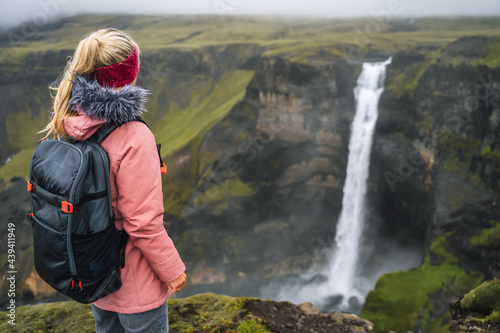 Woman with backpack and lilac jacket enjoying Haifoss waterfall of Iceland Highlands in Thjorsardalur Valley