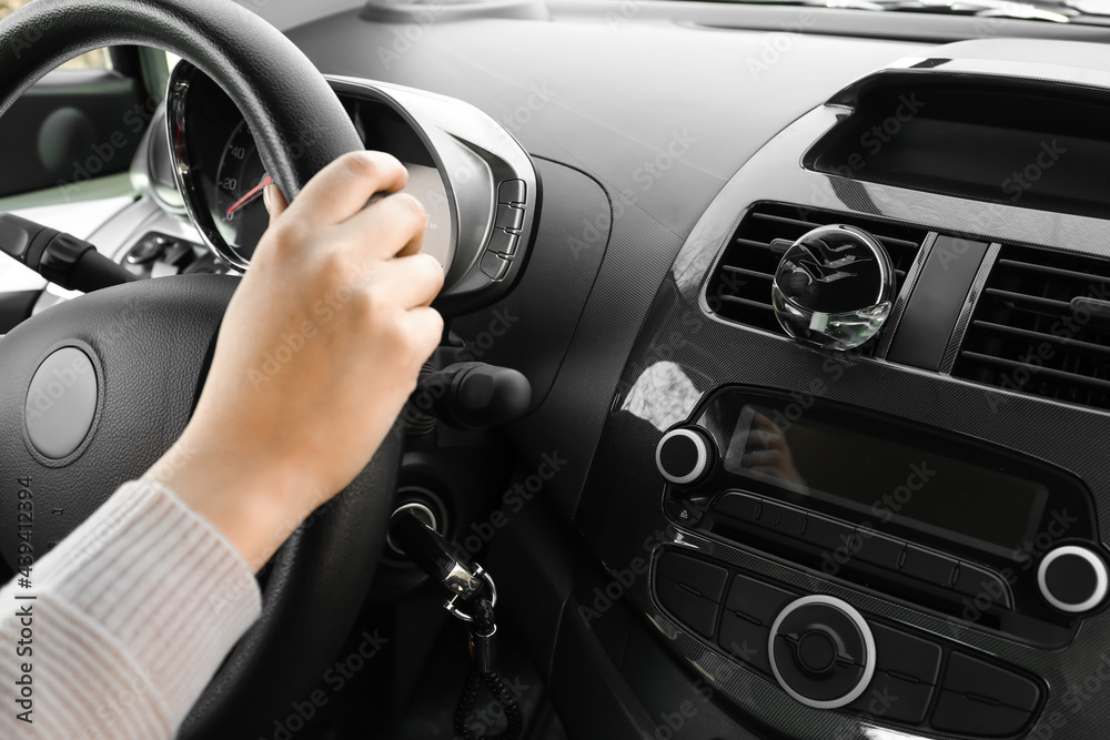 Young woman holding hands on steering wheel and air freshener hanging in car, closeup