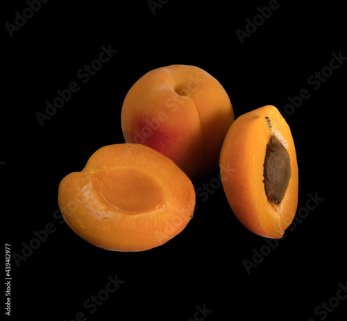 Ripe Apricot fruits, one whole apricot and two divided apricot pieces, on a black background in isolation