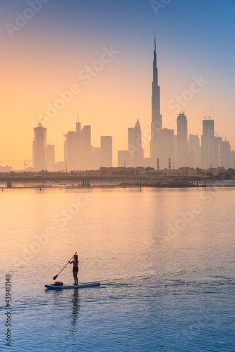 Photography girl glidies on surf board on the sea bay with view to morning Dubai