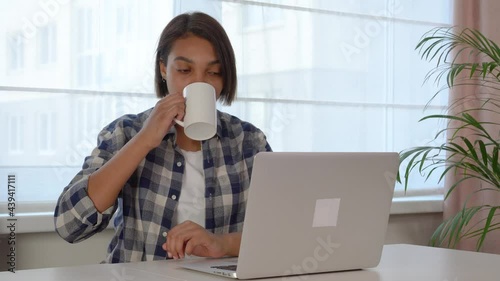 A young beautiful African-American woman looks at the laptop screen and communicates. Online video communication.