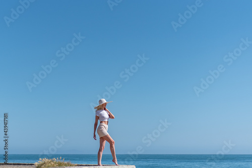 Beautiful blond hair female model clinging to hat while looking out into the large Pacific Ocean with horizon line down at her ankles.