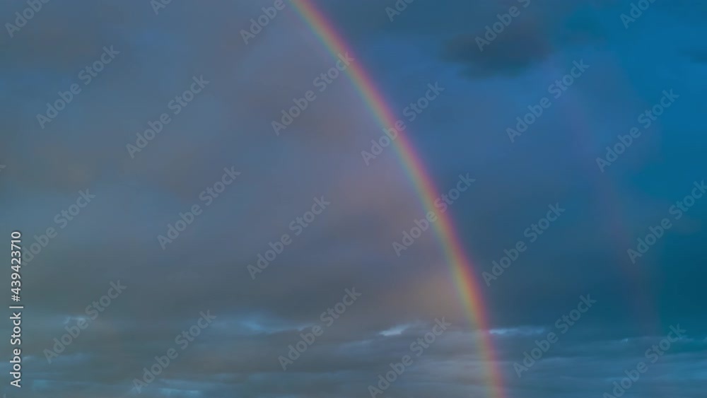 Time lapse of intense double rainbow on dark blue sky after rain. Timelapse,  light rays, copy space.
