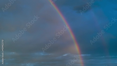 Time lapse of intense double rainbow on dark blue sky after rain. Timelapse,  light rays, copy space.