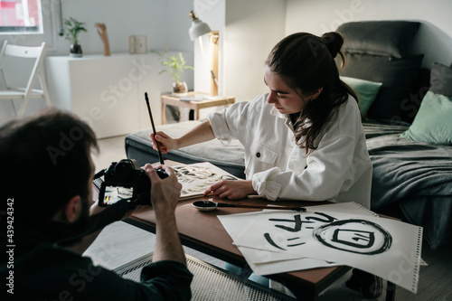 Young woman writing japanese kanji characters with a brush and ink and man filming her with video camera photo