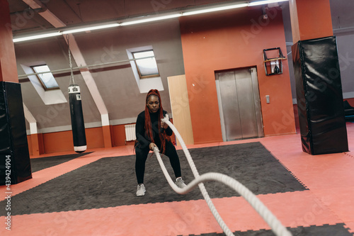 Determined black sportswoman doing exercises with battle ropes