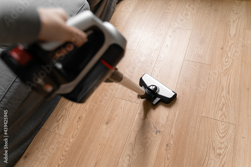 Cleaning wooden floor with wireless vacuum cleaner. Handheld cordless cleaner. Household appliance. Housework modern equipment