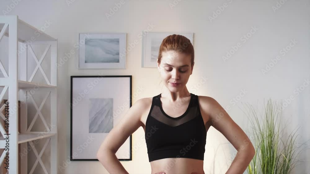 Home fitness. Physical exercise. Morning healthy routine. Active lifestyle. Inspired athletic woman in activewear enjoying stretching neck at light modern apartment interior.