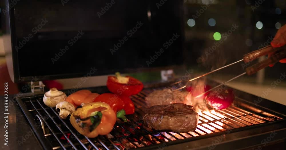 a man grilling meat steaks and vegetables on cozy rooftop patio at warm summer night, at home