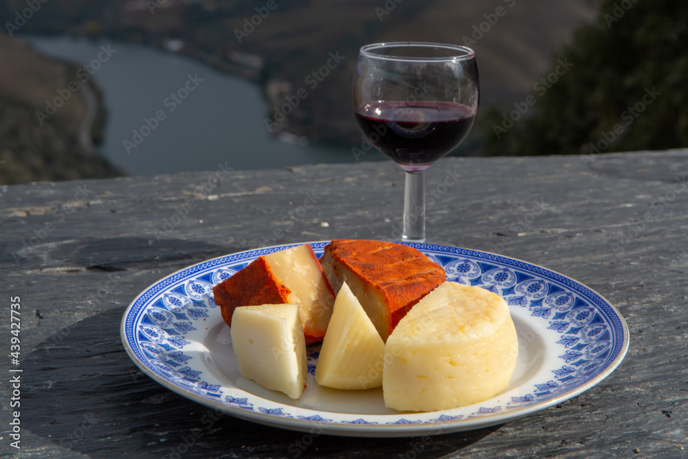 Taste of Portugal, variety of fortified port wines and goat and sheep cheeses, produced in Douro Valley with Douro river and colorful terraced vineyards on background in autumn, Portugal Taste of Portugal, variety of fortified port wines and goat and sheep cheeses, produced in Douro Valley with Douro river and colorful terraced vineyards on background in autumn, Portugal