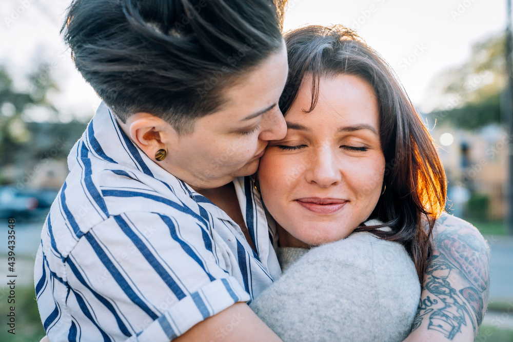 Lesbian woman hugging kissing wife on cheek Lesbian woman hugging kissing wife on cheek