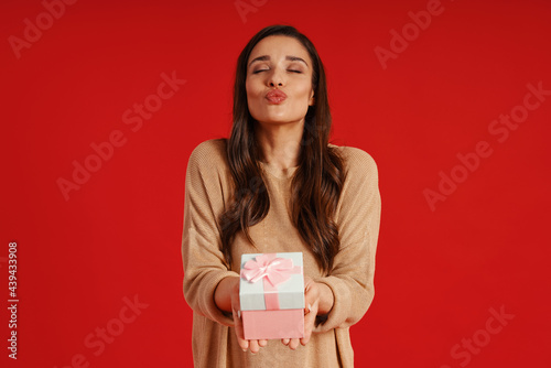 Attractive young woman in casual clothing blowing a kiss and holding gift box © gstockstudio