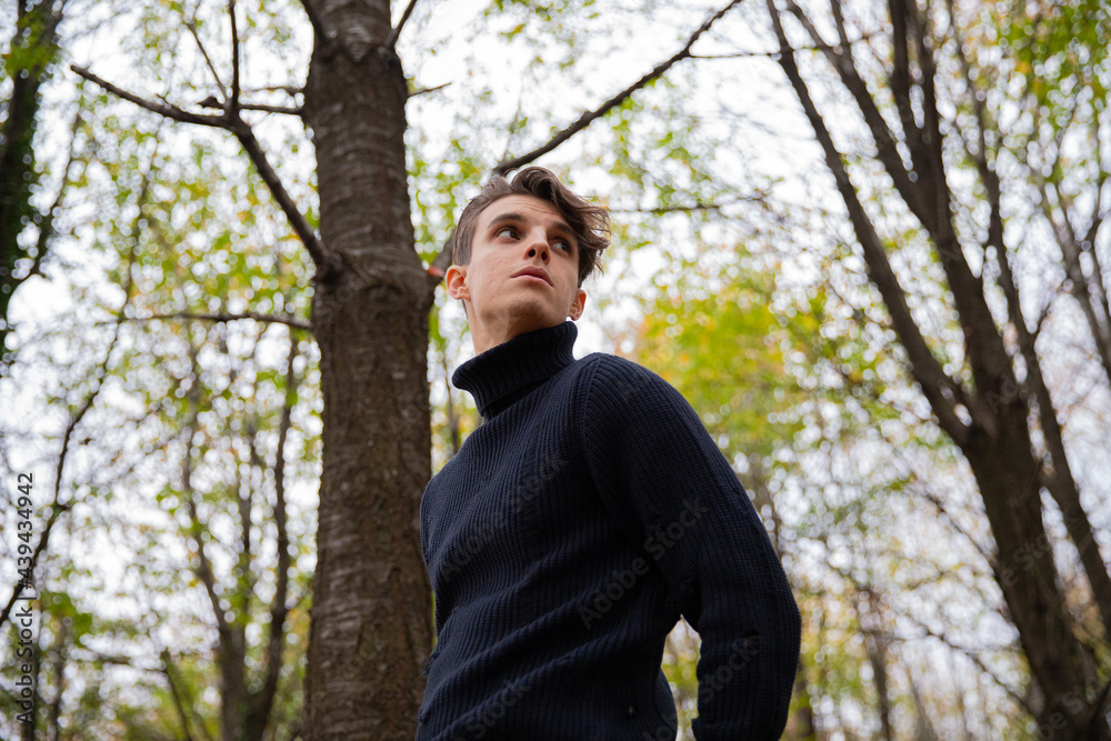 A man stands in an autumn forest, wearing a black wool sweater with a high collar and looking around.Thoughtful young male in a wood. A man stands in an autumn forest, wearing a black wool sweater with a high collar and looking around.Thoughtful young male in a wood.