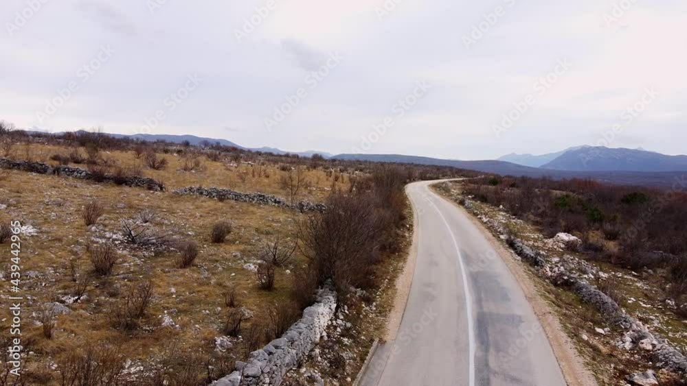 Empty asphalt road in highland among slopes with snowy rocks bare bushes and dry grass against distant mountains in winter aerial view Empty asphalt road in highland among slopes with snowy rocks bare bushes and dry grass against distant mountains in winter aerial view