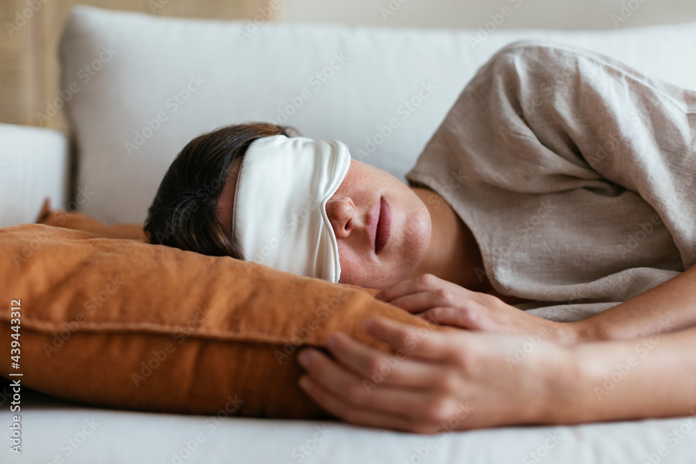 © BONNINSTUDIO/Stocksy - Woman in sleeping mask relaxing on sofa