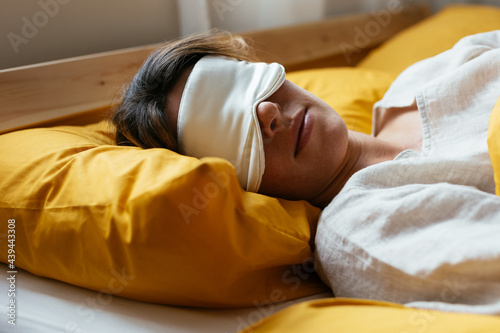 Tired woman in sleeping mask lying in bed